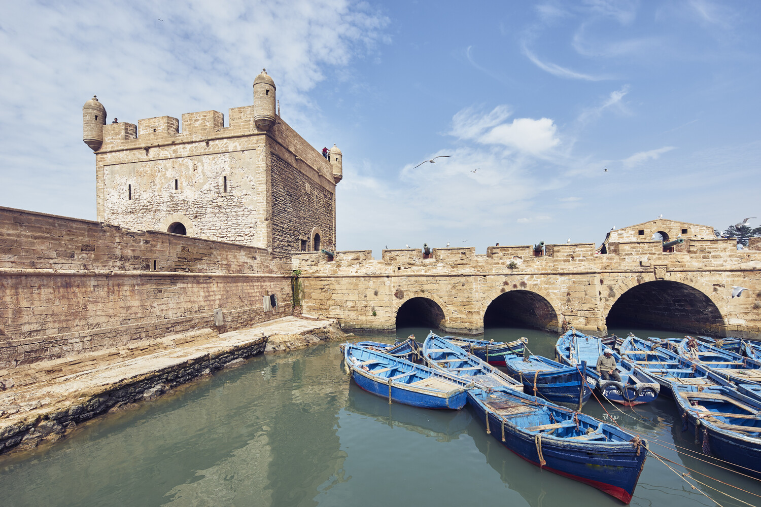 Blue boats floating by an ancient fortress under a clear sky.